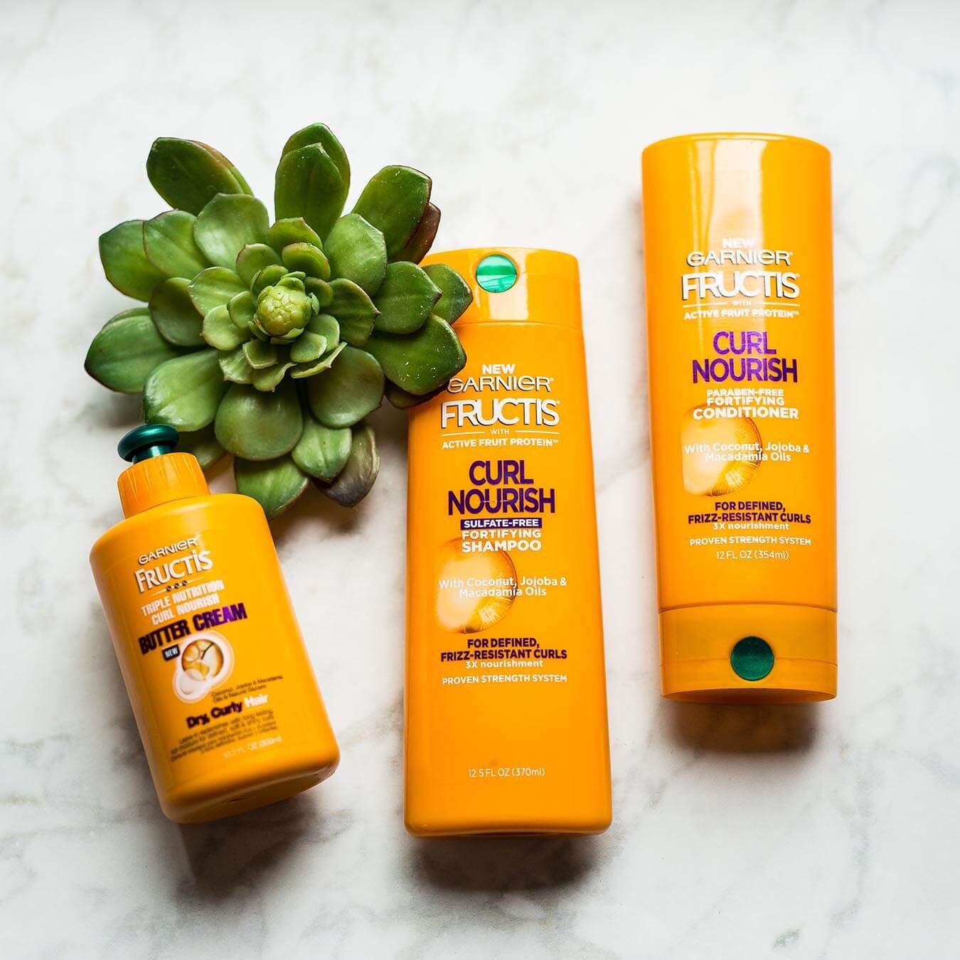 Garnier Fructis Curl Nourish Fortifying Shampoo, Fructis Curl Nourish Fortifying Conditioner, and Fructis Triple Nutrition Butter Cream laying on white marble next to a succulent.